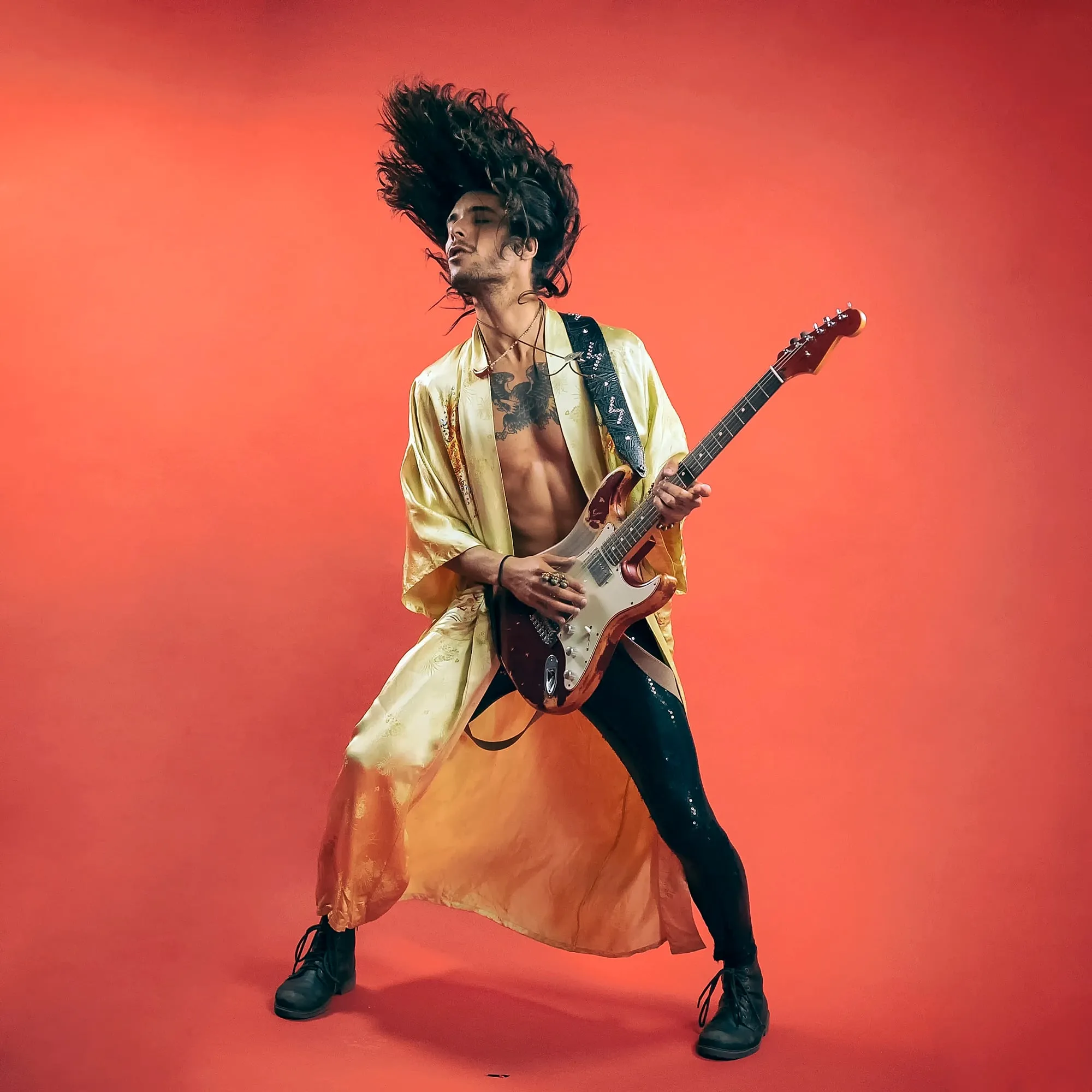 Guitarist in gold robe leaping against bold red background