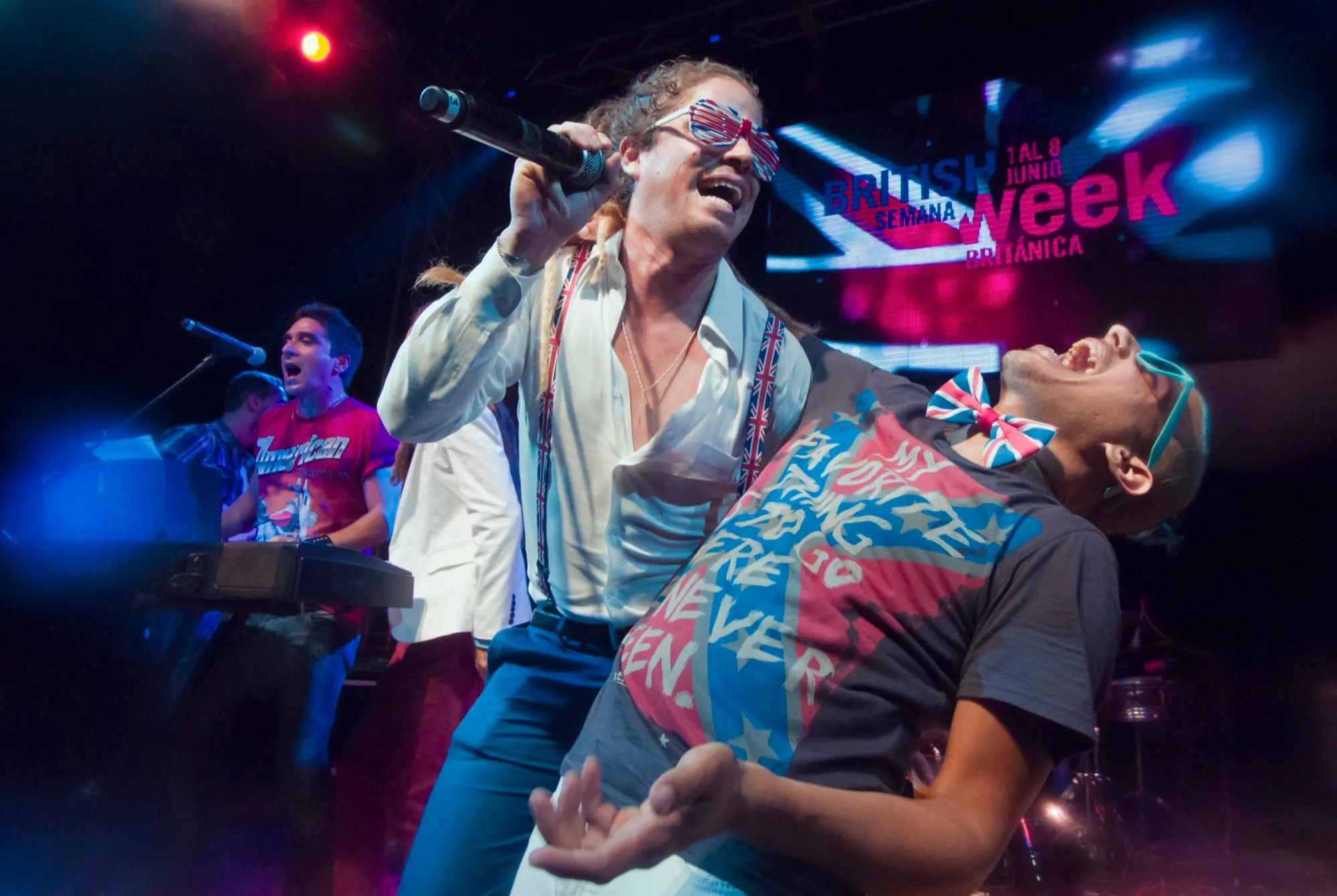 Two singers electrifying a packed stage under colorful concert lighting at British Week festival