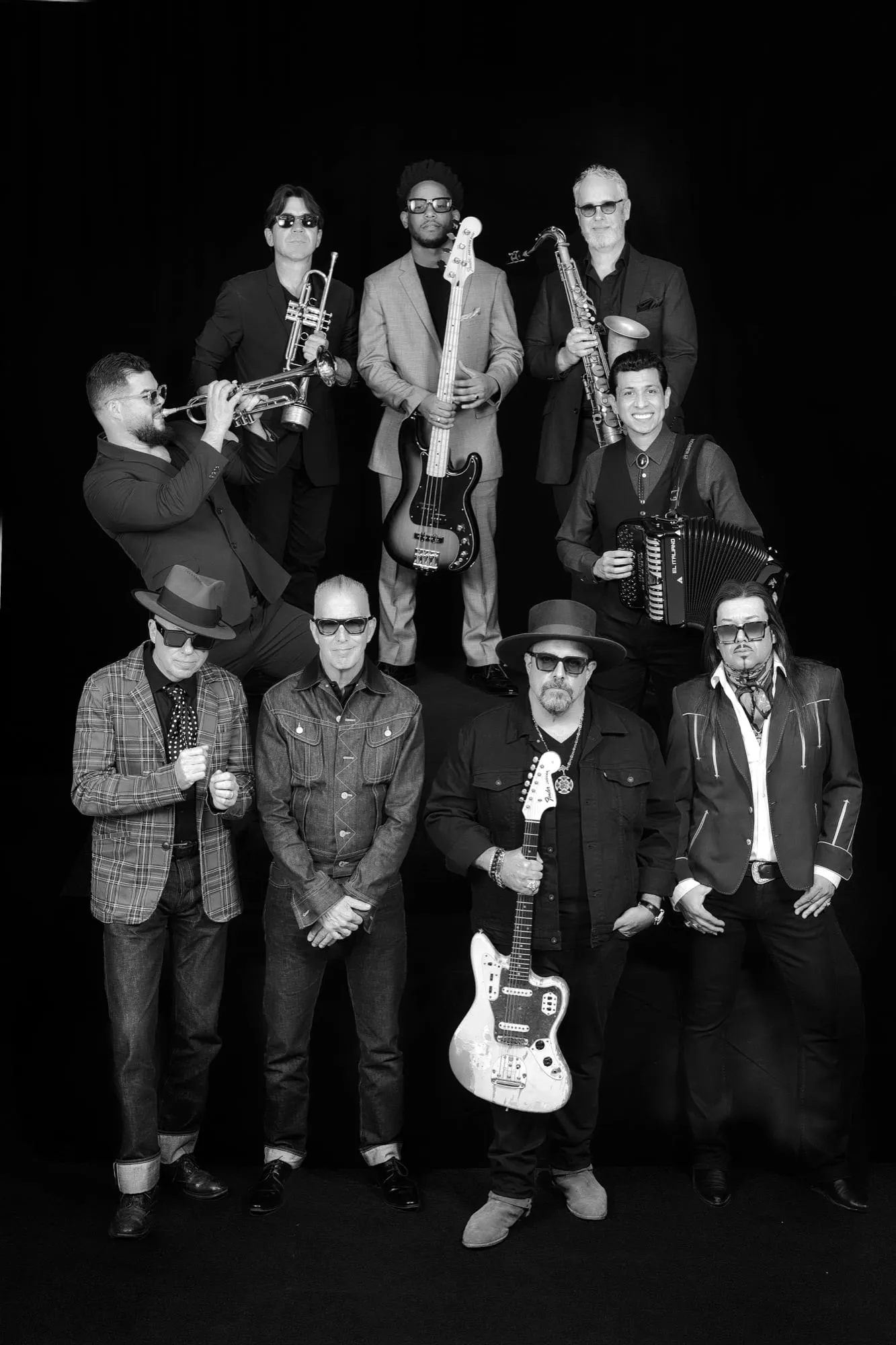 Nine-piece full band portrait in black and white, horns, guitar, bass, accordion