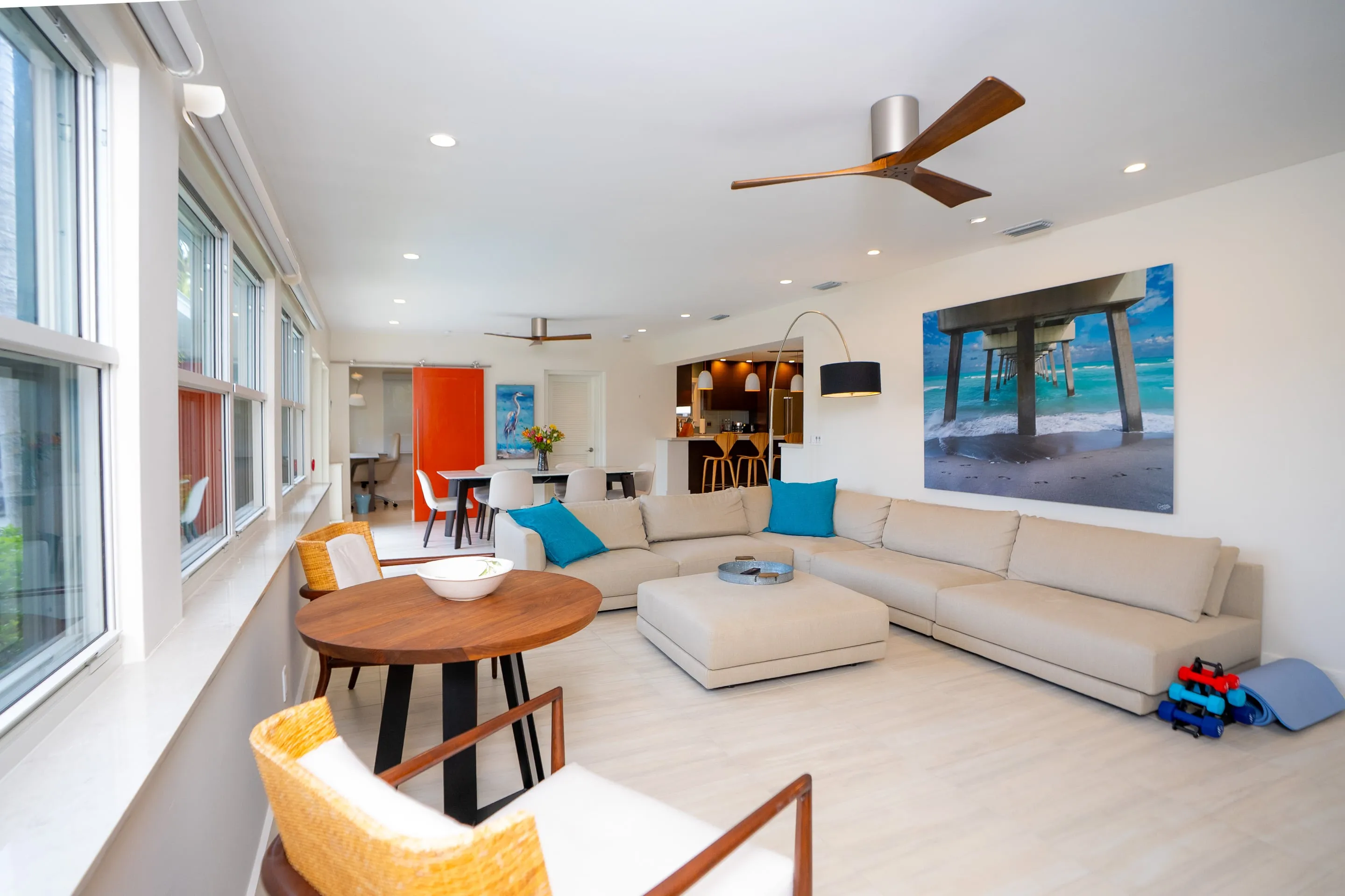 Open-plan vacation rental interior — coastal palette, hardwood floors, natural light through French doors