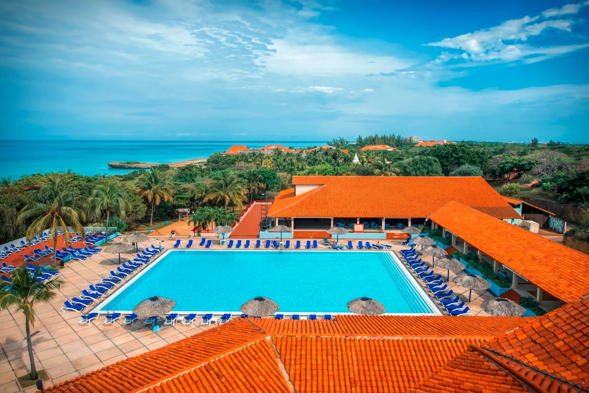 Aerial of oceanfront resort property — terracotta rooftops, large pool, turquoise water