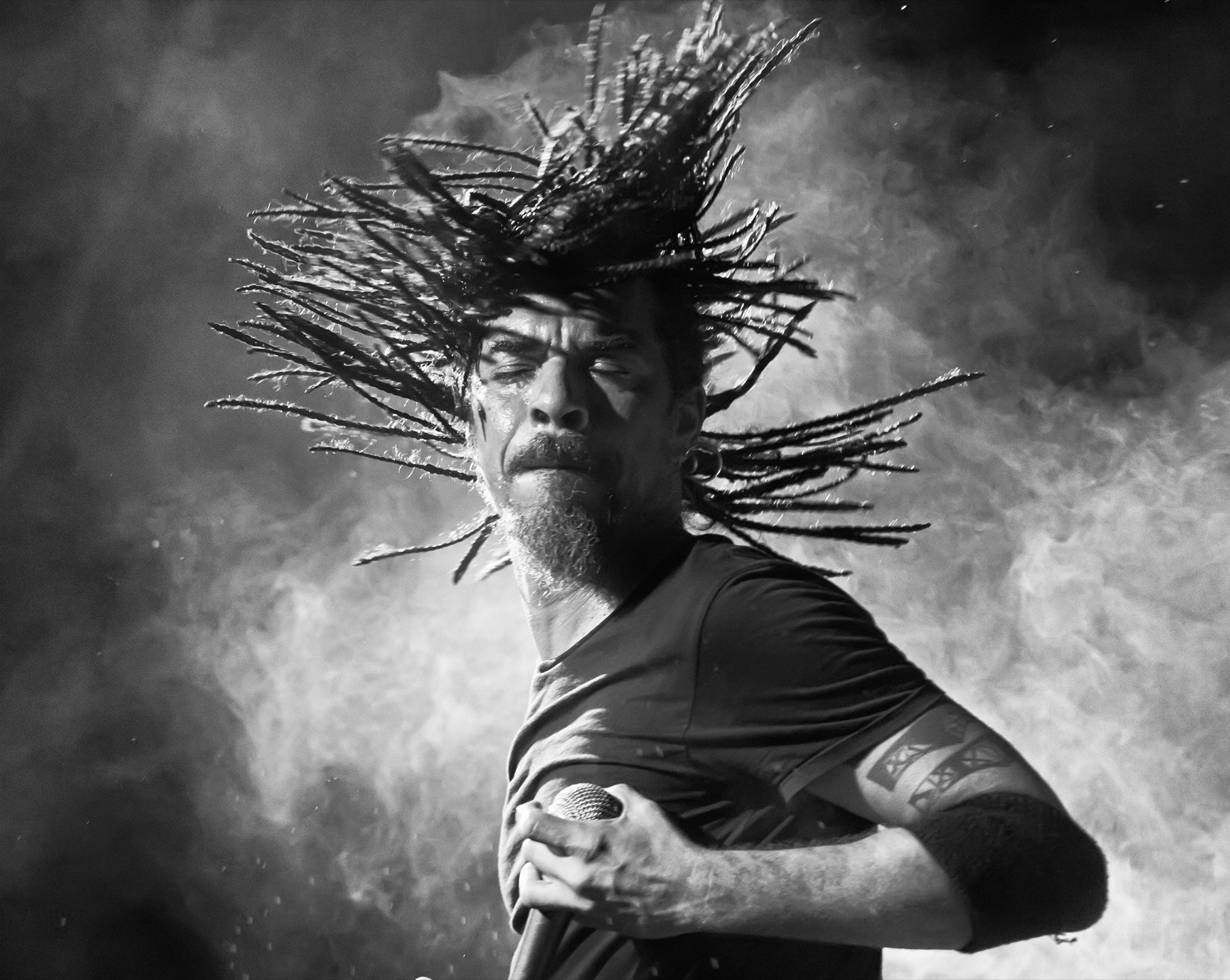 Singer in intense live performance, dreadlocks flying in stage smoke and dramatic lighting