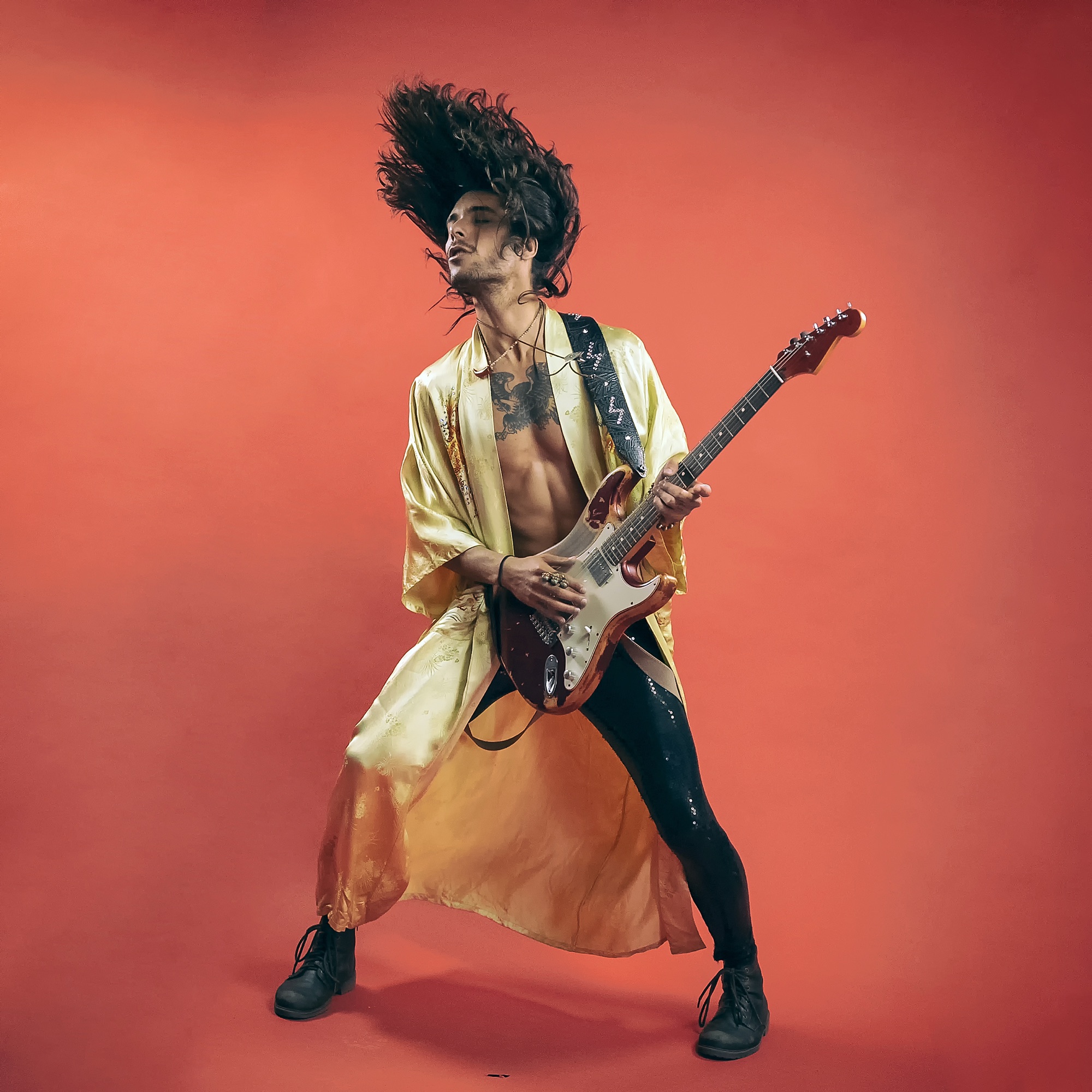 Guitarist in gold robe leaping against bold red background, electric guitar in full performance stance