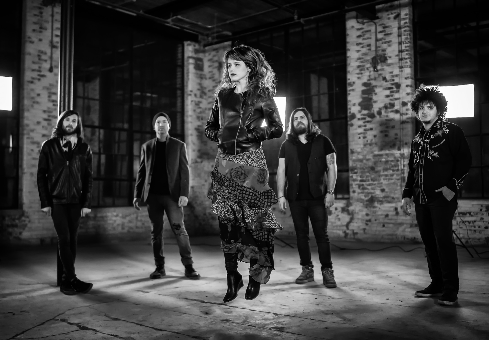 Five-piece band in dramatic black and white, lead singer suspended mid-leap in industrial warehouse