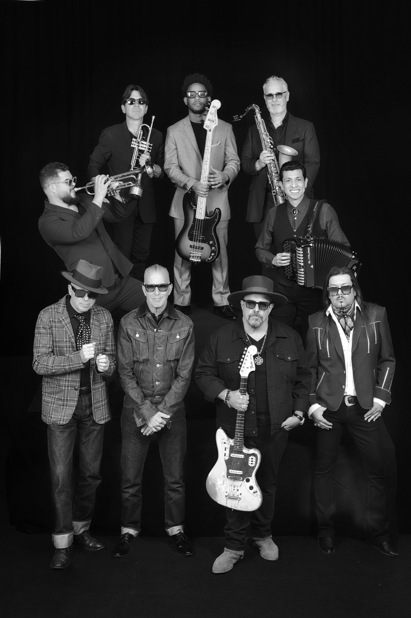 Nine-piece full band portrait in black and white, members with horns, guitar, bass, and accordion