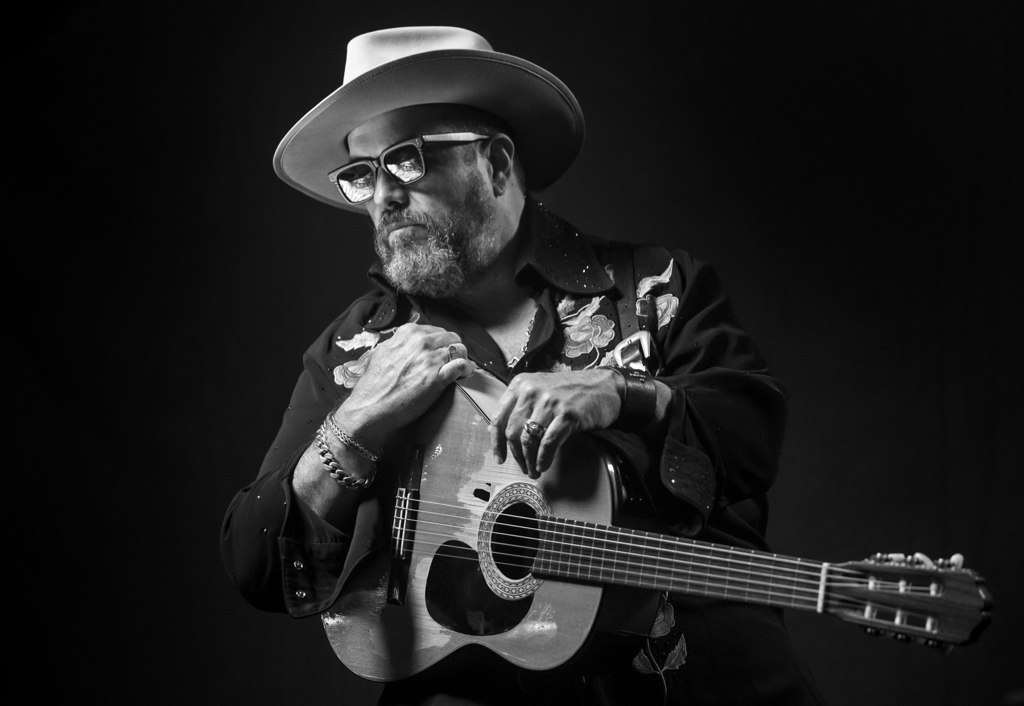 Veteran guitarist with cowboy hat and acoustic guitar in intimate black and white studio portrait