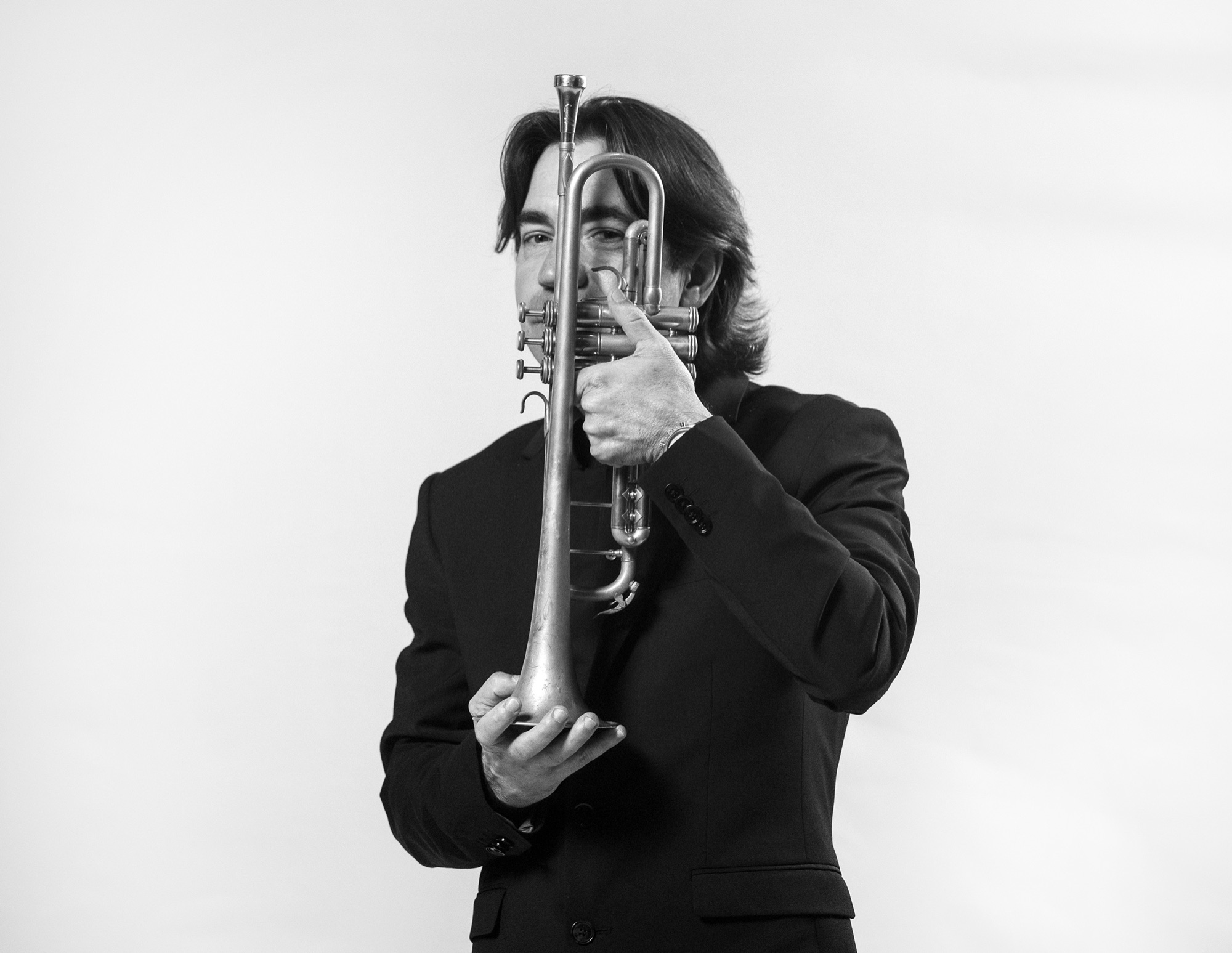 Musician holding trumpet obscuring face in moody black and white studio portrait