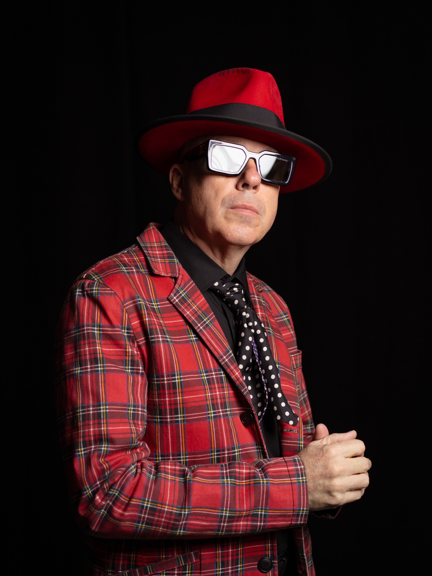 Boldly dressed musician in red plaid suit and red fedora, character portrait against black background