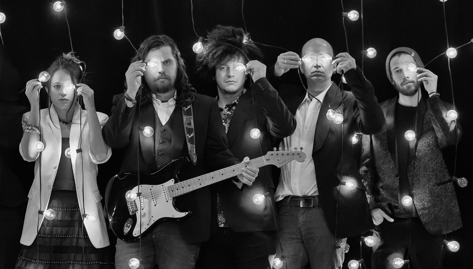 Five-piece band holding glowing lightbulbs in creative black and white conceptual band portrait